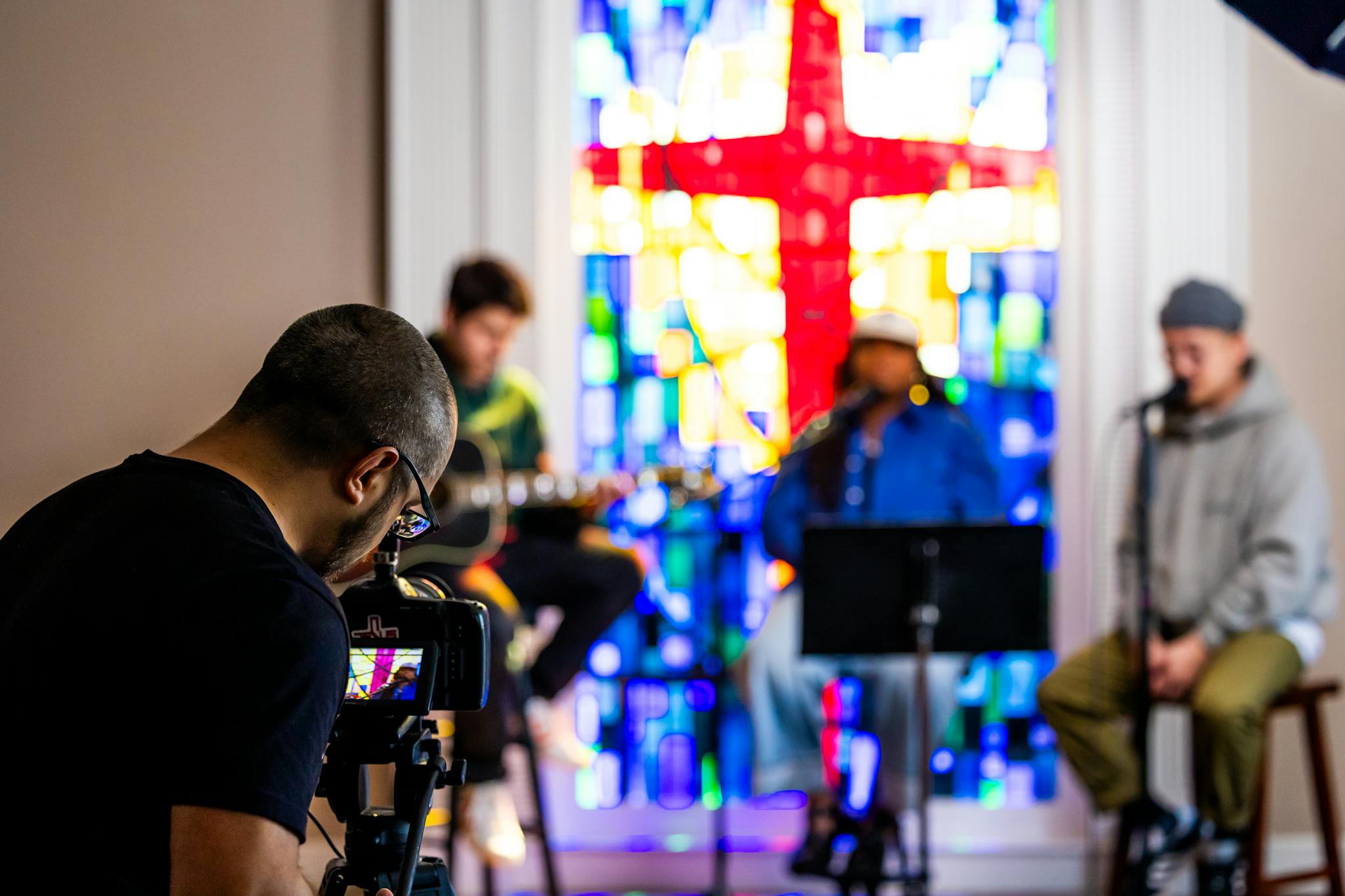 Musicians performing in front of vibrant stained glass during a church recording session.